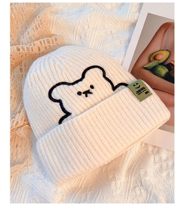 Detailed embroidery of a black bear on a white knit beanie with a green label