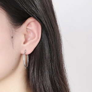 Silver twisted rope hoop earrings worn by a model with a minimalist high-shine finish