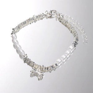 Detail of pearl bracelet with faceted silver beads and a shiny bow charm on mirror
