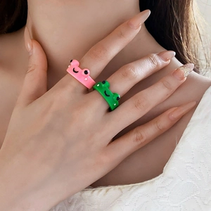 Close-up of cute pink and green resin frog rings worn on a hand over white lace