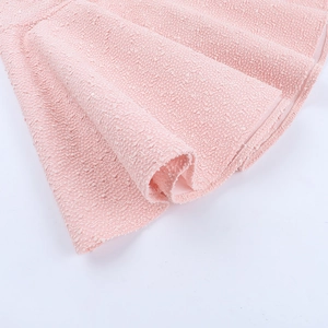 Detailed view of pink tweed dress showing the textured fabric and wavy hemline edges