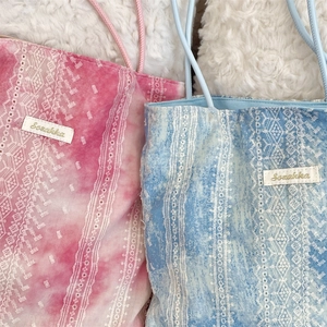 Detail of tie-dye lace tote bag with floral embroidery and brand label on plush fabric