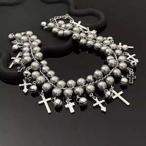 Macro detail of gothic gray pearl multilayer bracelet with silver cross and bell charms