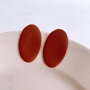 Close-up of reddish-brown oval enamel earrings with gold edges on a ceramic plate