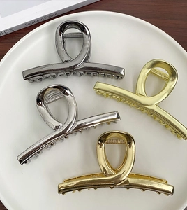 Flat lay of four minimalist gold and silver large metal hair claws on a white tray