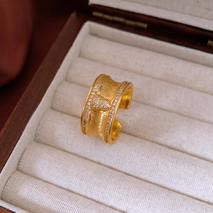 Dettaglio macro dell'anello largo dorato con texture spazzolata e cuore di zirconi