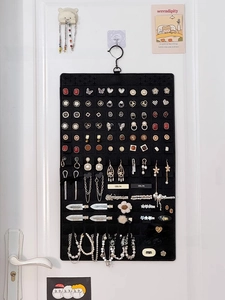 Hanging black felt jewelry organizer with hooks for earrings and necklaces on a white door