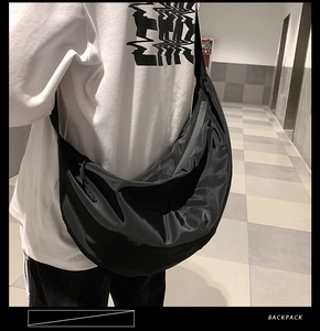 Close-up of large black nylon crescent crossbody bag worn over shoulder on white shirt