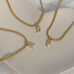 Détail de colliers en acier titane doré avec pendentifs lettres D N F en zircone