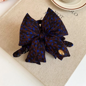Detail of a large leopard print fabric bow hair claw clip with golden metal love tag