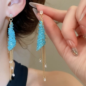 Close-up of blue beaded triangle earrings with gold chain tassels and zircon details