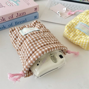 Quilted checkered drawstring camera pouch on a desk with laptop and headphones