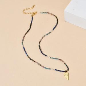 Bohemian beaded tourmaline necklace with gold heart evil eye pendant on beige background