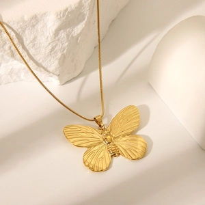 Detailed close-up of a golden stainless steel butterfly pendant on a textured rock base
