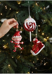 Festive red glitter elf, lollipop, and shoes hanging on a lit Christmas tree branch