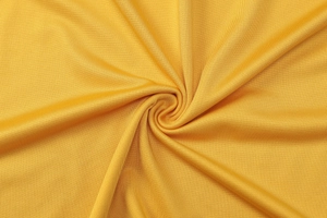 Macro shot of yellow knitted fabric showing soft texture and detailed stitch pattern