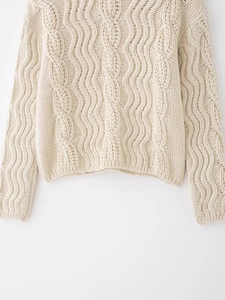 Detail of cream cable knit sweater showing textured weave and ribbed hem craftsmanship