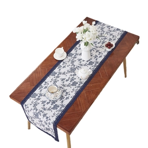Blue and white porcelain style linen table runner with lace trim on a wooden table