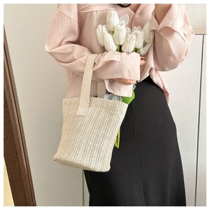 Detail of a beige straw bucket bag featuring a refined herringbone weave and leather handles