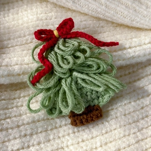 Close-up of a handcrafted green knitted Christmas tree hair clip with a red bow and brown trunk