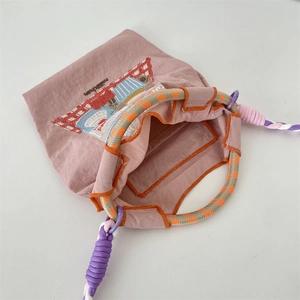 Gros plan d'un mini sac rose brodé avec des poignées en corde tissée multicolore