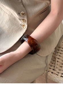 Close-up of a wide amber textured cuff bracelet styled with a beige blazer sleeve