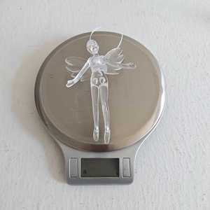 Close-up of a clear acrylic angel ornament on a scale showing 21.7g weight detail
