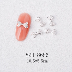 Detail of silver alloy bow nail charms with white pearls on a light pink nail tip