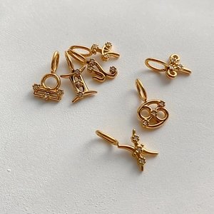 Detalle de dijes del zodiaco chapados en oro con incrustaciones de pedrería para joyería DIY