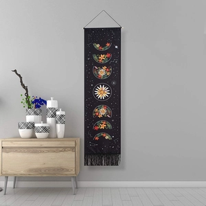 Bohemian moon phase tapestry with floral designs and black tassels on a grey wall