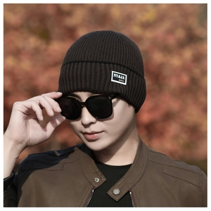 Detailed close-up of dark brown knitted beanie with fashion patch on outdoor model