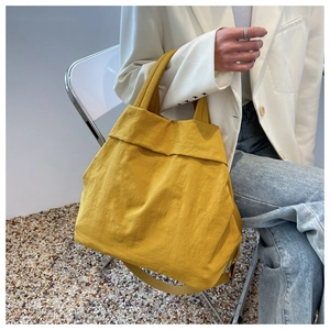 Close-up of a vibrant mustard yellow nylon tote bag styled with a casual white blazer
