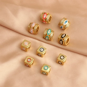 Perles Evil Eye dorées de formes cylindriques et cubiques sur un tissu en soie rose