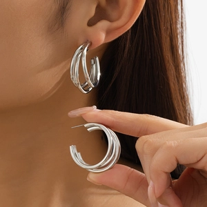 Close-up of triple-layered silver geometric C-shape hoop earrings on a model's ear