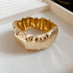 Gros plan d'un bracelet manchette doré large avec une texture froissée irrégulière