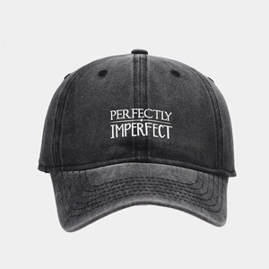 Detailed close-up of 'PERFECTLY IMPERFECT' embroidery on a washed grey denim baseball cap