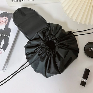 Flat lay of black drawstring makeup bag with beauty accessories on white background