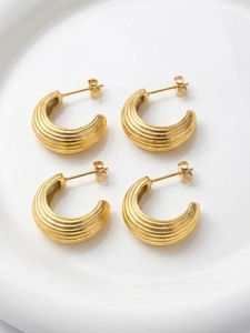 Gros plan de boucles d'oreilles en C en acier doré avec détails texturés à rayures