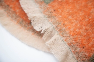 Detailed macro view of orange and beige boucle plaid scarf with soft fringe edges