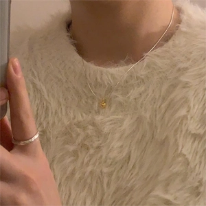 Detail of minimalist gold heart pendant necklace worn on a white textured sweater
