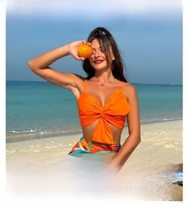 Detail of orange twist-knot bikini top and high-waisted tropical print bottoms at beach