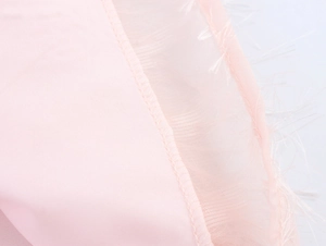 Dettaglio del tessuto rosa con rete traslucida e rifiniture in frange di piume bianche