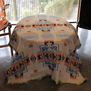 Bohemian style woven camping blanket with geometric patterns and fringe edges on a table
