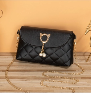 Detail of black quilted crossbody bag featuring cat-shaped metal clasp and twin pearls