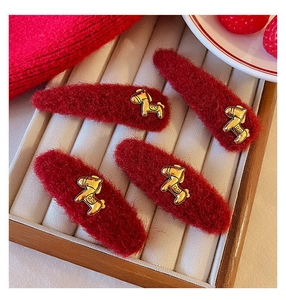 Vista macro di quattro fermagli per capelli in peluche rosso con ciondolo pony dorato