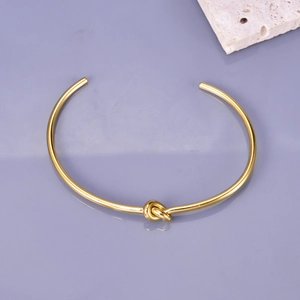 Detail view of a gold-plated stainless steel knot bracelet with an open cuff design