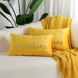 Macro shot of yellow velvet pillow with silver HELLO Sunshine text on a cozy white sofa