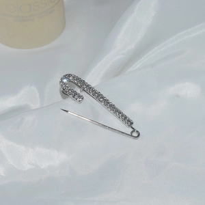 Detailed view of silver safety pin brooch with sparkling rhinestones on silk fabric