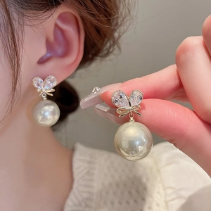 Close-up of elegant pearl drop earrings with heart-shaped crystal and gold bow details