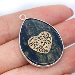 Macro detail of teardrop stone pendant with golden hollow heart and silver metal frame